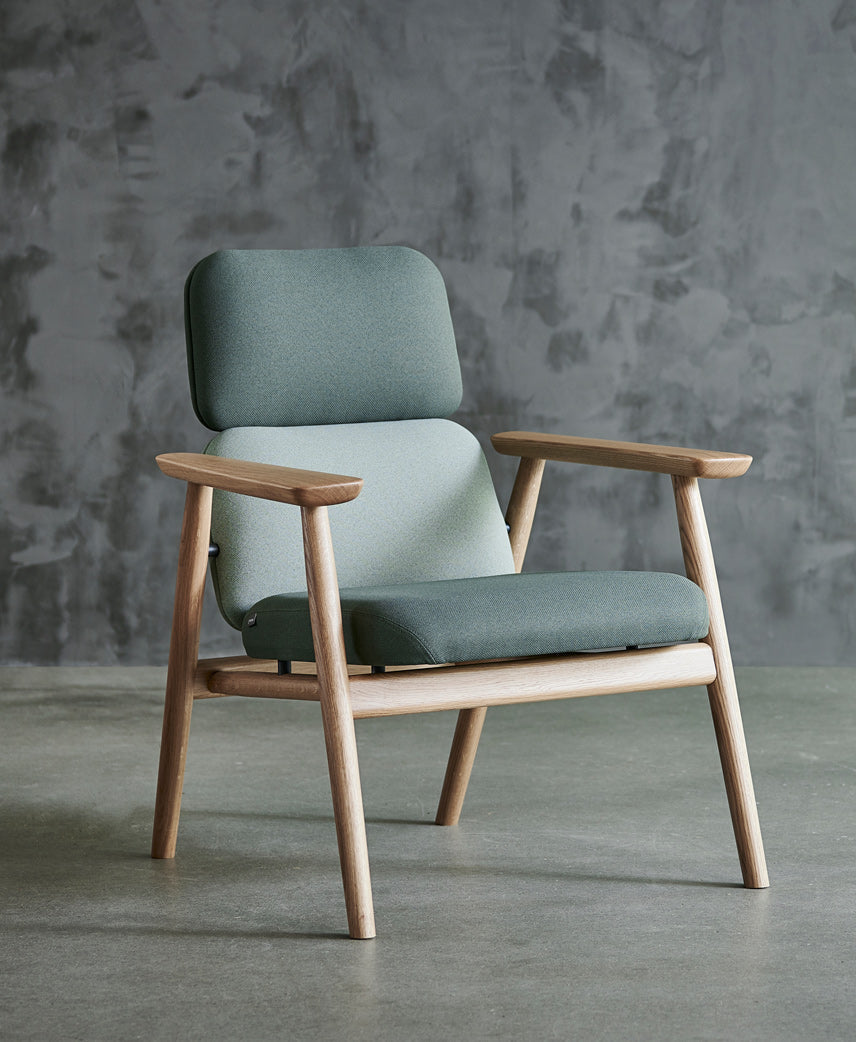 Lænestol / Loungestol, model Bear L, stel i massiv natur eg og polster i to nuancer grøn tekstil, den står på beton gulv foran rustik væk