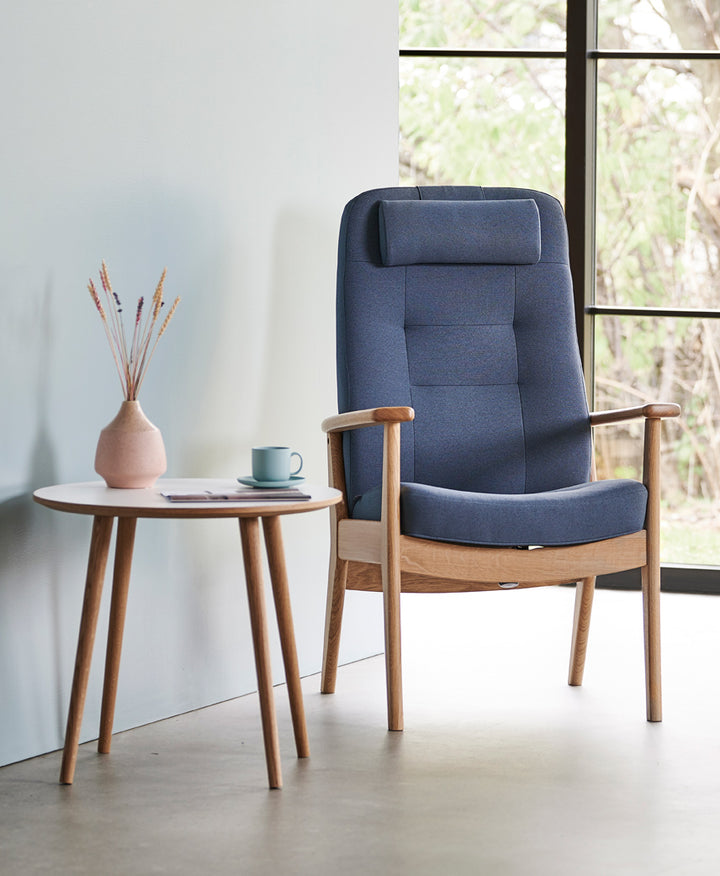 Lænestol med lille ryg, model Plus 5920, stel i natur eg og polster i lys støvet blå, stående i lyst miljø.
